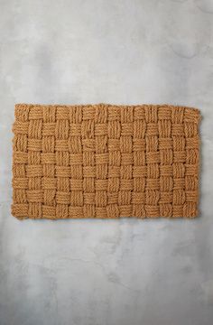 a brown door mat with braiding on the front and back sides, against a gray wall