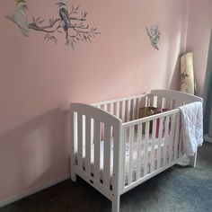 a white crib in front of a pink wall with birds painted on it