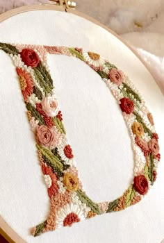 a close up of a embroidery on a white cloth with a cross stitched letter d