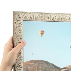 a person holding up a framed photograph with hot air balloons in the sky