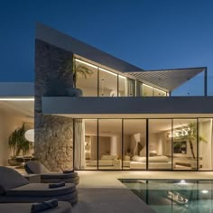 a modern house with an outdoor pool and lounge area at night, lit up by lights on the windows