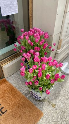 pink tulips are in a vase on the floor next to a welcome mat