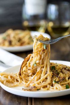 a fork full of spaghetti being lifted from a white plate with another plate in the background