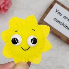 a hand holding up a yellow felt sunflower with eyes and eyelashes, next to a sign that says you are sunshine