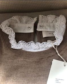 a sweater with white lace on it and a tag attached to the front of it