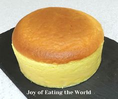 a round yellow cake sitting on top of a black plate with the words joy of eating the world