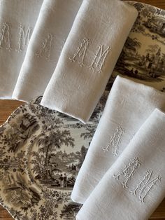 four white linen napkins with embroidered monogrammed names on them sitting on a table