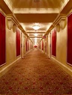 a long hallway with red doors and carpeted flooring on both sides, leading to another room