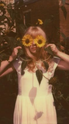 a woman with sunflowers on her face standing in front of a tree and building