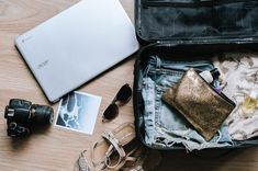 an open suitcase sitting on top of a wooden floor next to sunglasses and other items