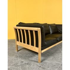 a black leather couch sitting on top of a gray floor next to a yellow wall