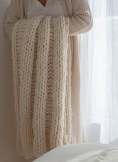 a woman is holding a blanket over her head while standing in front of a window