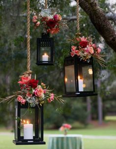 three hanging lanterns with flowers and candles on them are hung from a tree in the woods