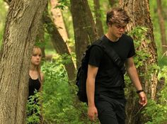 two people walking through the woods with backpacks on their back and one person looking at something