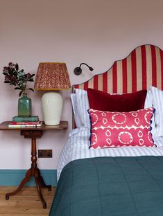 a red and white headboard sitting next to a bed in a room with pink walls