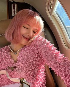 a woman with pink hair sitting in the back seat of a car and smiling at her cell phone