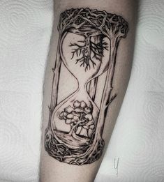 an hourglass tattoo on the arm with trees and mushrooms in it's frame