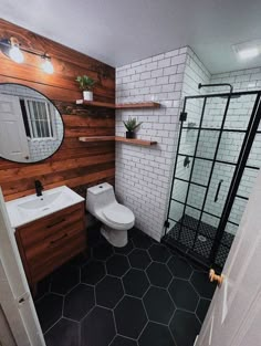 a white toilet sitting next to a walk in shower under a bathroom mirror on top of a wooden shelf