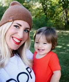 a woman and her child are posing for a photo in the grass with trees behind them