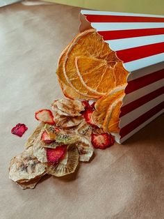 orange slices and strawberries in a striped paper box next to dried fruit on the table