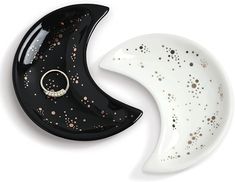 two black and white moon shaped dishes with gold speckles on the top one has a ring in it's mouth