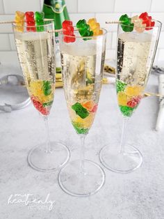 three champagne flutes filled with gummy bears and candy on a marble counter top next to a bottle of champagne