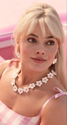 a woman with long blonde hair is standing in front of a pink hoop and smiling at the camera