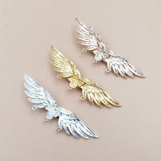 three gold and silver angel wings on a beige background, one is facing the opposite direction