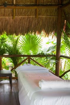 two beds with white sheets and pillows in front of some palm trees on a deck