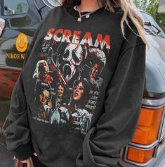 a woman standing next to a car wearing a sweatshirt with the words scream on it