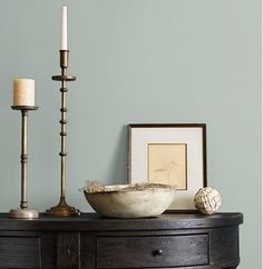 a table with a bowl and two candles on it next to a framed photograph, candle holder and other items