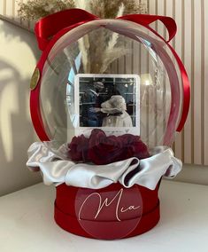 a snow globe with a photo inside and red ribbon around the base, sitting on a table