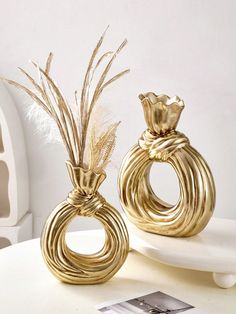 two decorative gold vases sitting on top of a white table