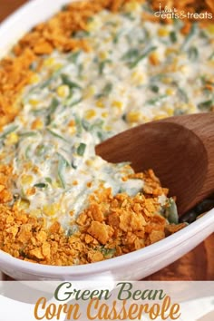 a casserole dish filled with green beans, corn and cheese on a wooden spoon