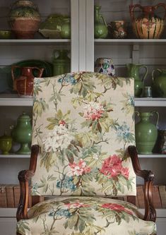 an upholstered chair in front of shelves with vases