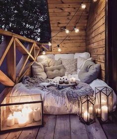 an outdoor seating area with candles and pillows on the floor, surrounded by wood planks