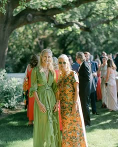 two women standing next to each other in front of a group of people on grass