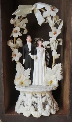 a wedding cake topper in a wooden box with flowers on the bottom and a bride and groom standing next to each other