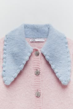 a pink and blue sweater with buttons on the collar