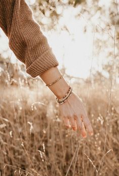 a woman's hand reaching for something in the tall grass with trees in the background