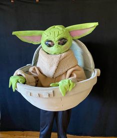 the child yoda doll is sitting in an egg shell with his hands on his hips