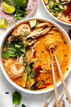 two bowls filled with noodles and vegetables next to chopsticks on a white table