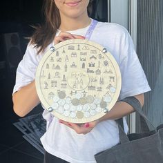 a woman holding up a wooden plate with various symbols on it, in front of a window