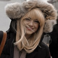 a woman with blonde hair wearing a fur hat and black jacket, smiling at the camera