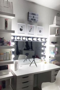 a white desk topped with lots of drawers under a lighted mirror next to a chair