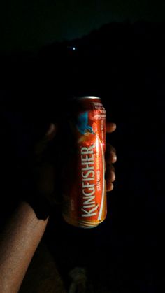 a person holding up a can of beer in the dark