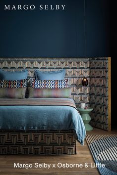 a bed with blue sheets and pillows in a dark room next to a rug on the floor