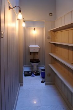 an empty bathroom with shelves and lights on the wall, along with a toilet in the corner