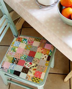 a bowl of oranges sitting on top of a table next to a cloth covered chair