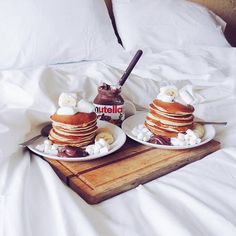 two pancakes on plates with marshmallows and chocolate sauce in the middle sitting on a bed